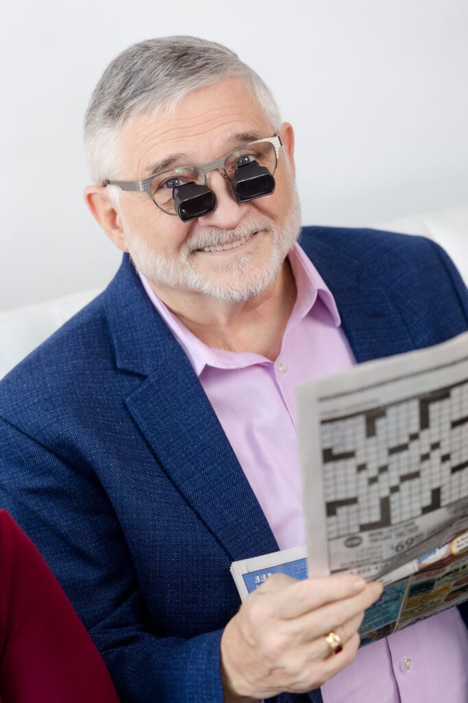 A man wearing low vision glasses looking up from the newspaper