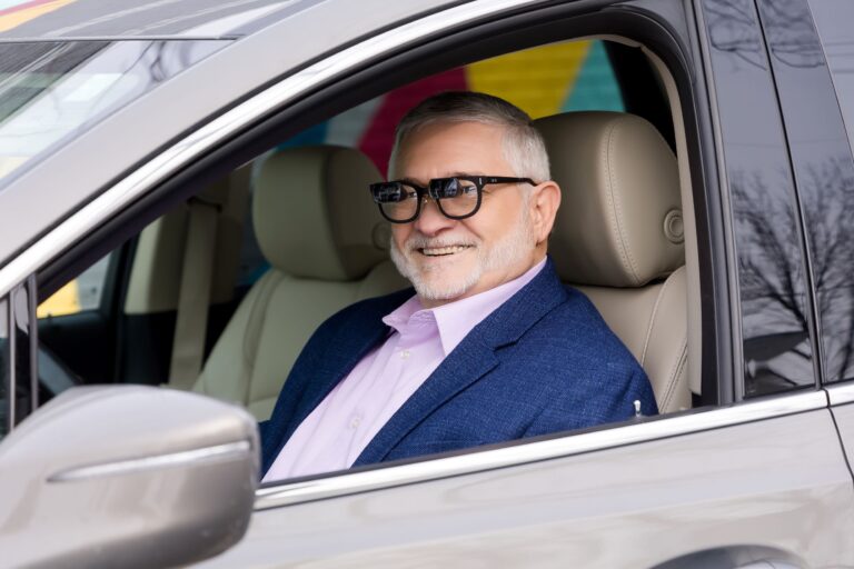 Smiling man driving a car with low vision glasses on