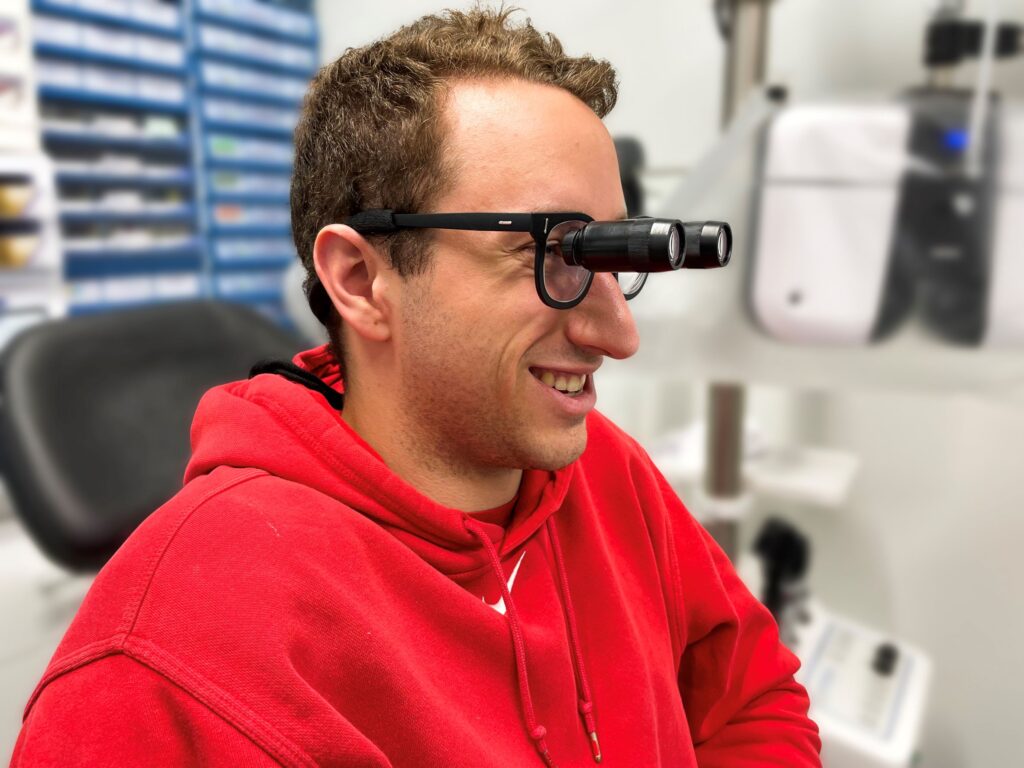 Young man smiling wearing low vision glasses