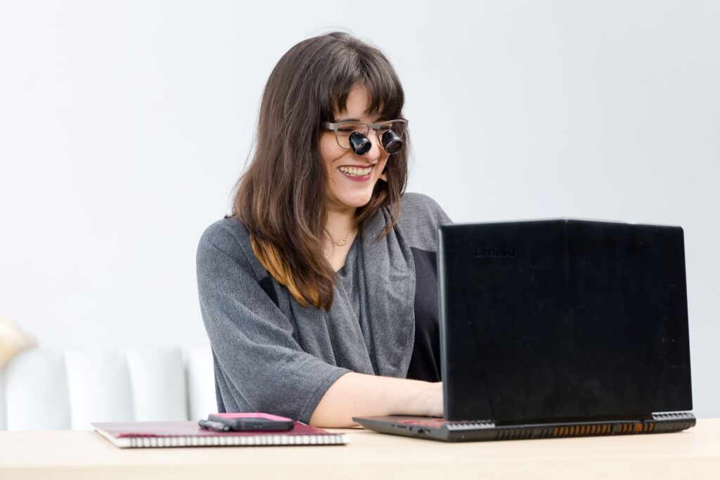 Woman smiling in low vision glasses working on a laptop