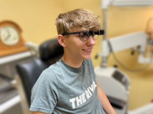 A smiling young boy wearing low vision glasses in a doctor's office