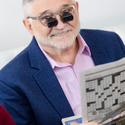 A man wearing low vision glasses looking up from the newspaper